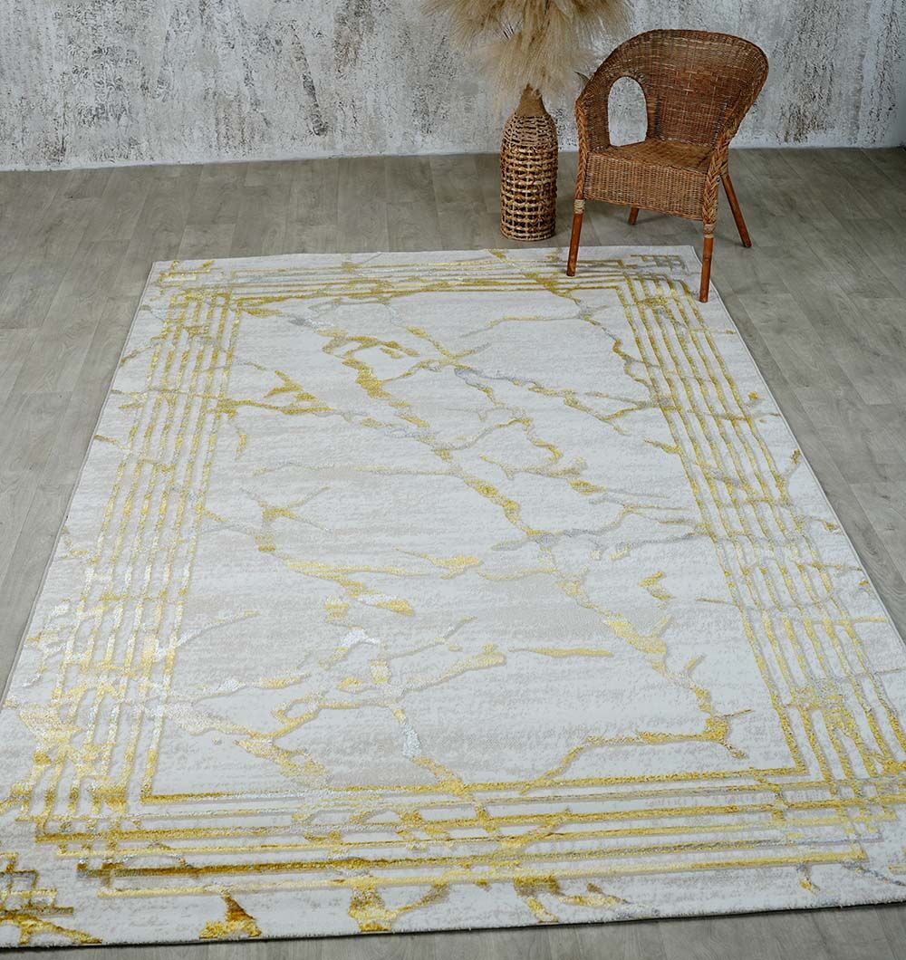 The RAMSHA HOME Ivory & Gold Machine Made Turkish Area Rug - NK82A MADRID with a marble pattern and geometric border is laid on a grey wooden floor, accompanied by a wicker chair and vase.