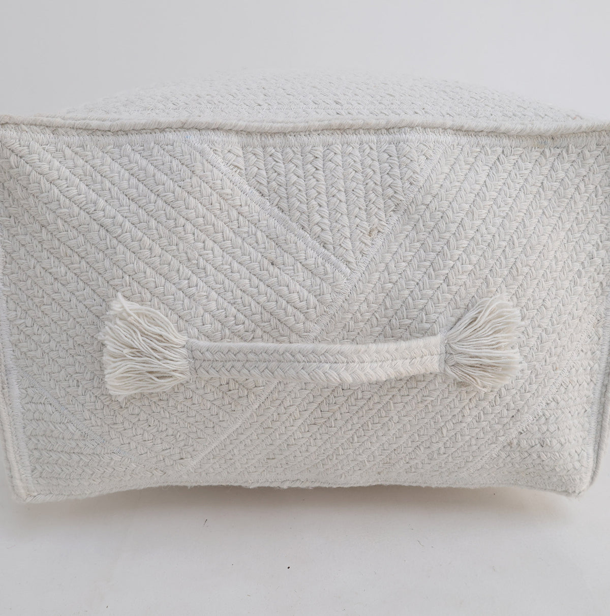 The RAMSHA HOME Bleach color Floor Square Pouf with Handle PF 088 features a textured, off-white woven design with a convenient handle and tassels on one side. Its bleach-colored tones make it an ideal decorative accent piece that stands out beautifully against a plain white background.