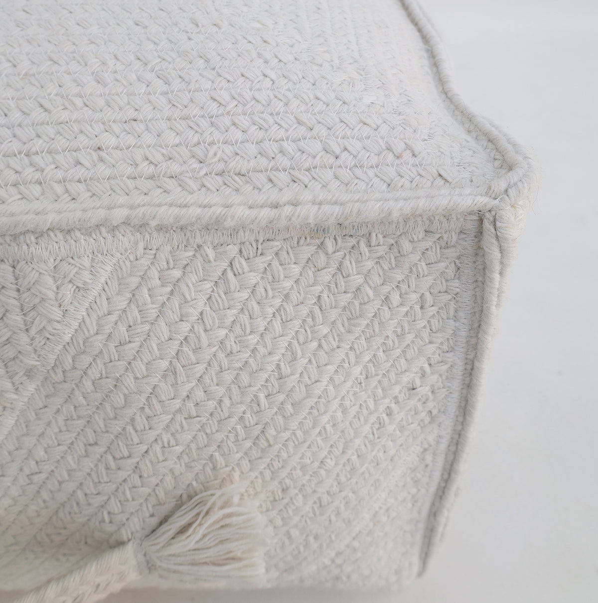 Experience the subtle elegance of the RAMSHA HOME Bleach color Floor Square Pouf with Handle PF 088—featuring close-up details of its textured, off-white woven fabric and distinctive braided pattern. This stylish pouf is finished with a small corner tassel and designed for both extra seating and a modern touch to your interiors.