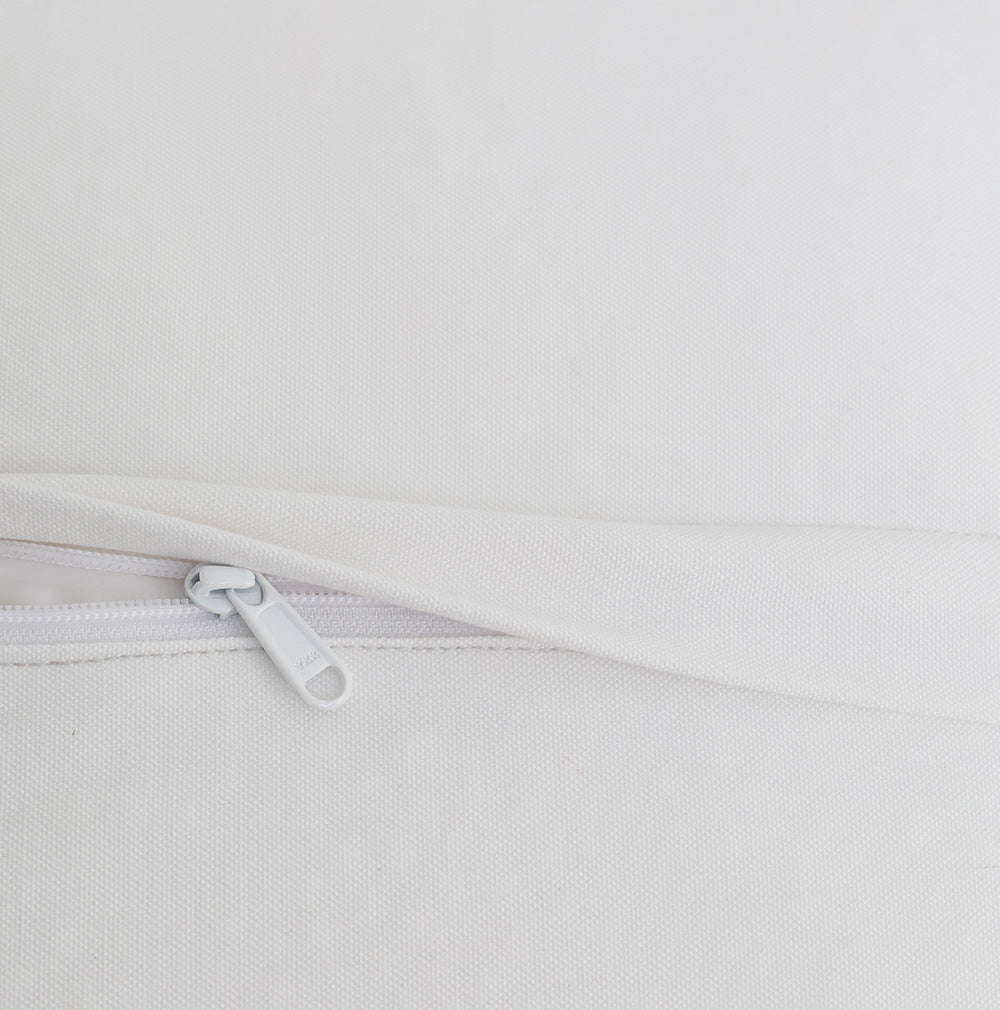 A close-up of a white pillow with a visible white zipper, partially unzipped to reveal the textured fabric cover—perfectly complementing the RAMSHA HOME Bleach color Floor Square Pouf with Handle PF 088 as an elegant decorative accent piece.