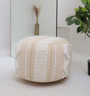The RAMSHA HOME Boho Modern Round Pouf With Insert PF 090, cream-colored with textured white stripes and bobbles, adds extra seating on a white floor. Behind it, a mirror reflects a vase of dried grasses and a nearby green plant.