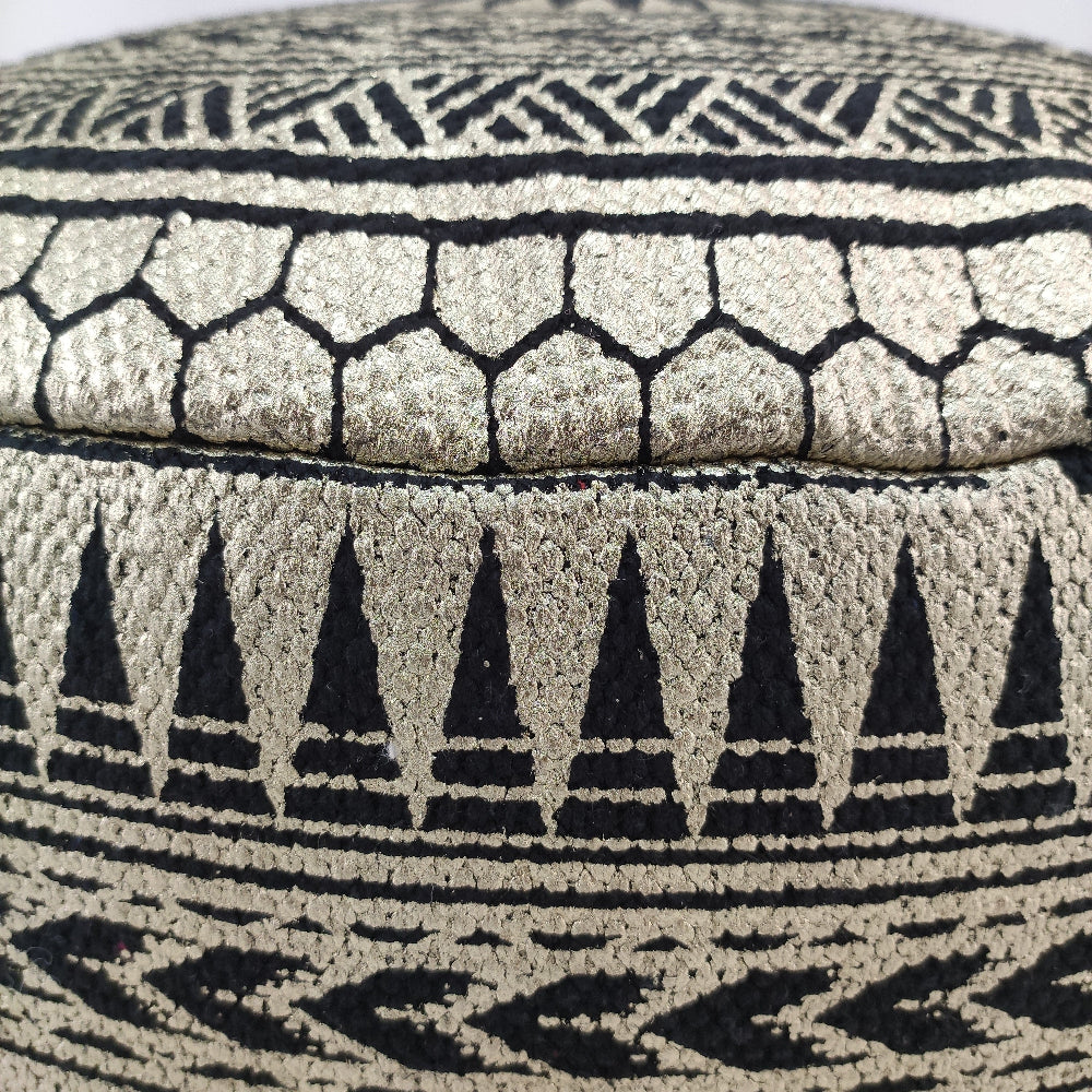 Close-up of the RAMSHA HOME Cotton Pouf Black And Gold With Leather Handle PF-092, featuring textured cotton with black and gold geometric patterns. The curved pouf includes a leather handle for easy portability.