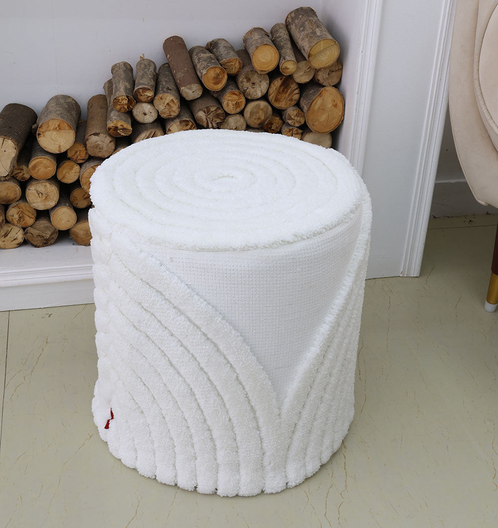 The RAMSHA HOME Luxury Handmade Pouf with Thermocol Bean Bag Insert PF-148, featuring a white textured finish and towel-like design, sits by the fireplace and beige chair, adding a premium touch to your home décor.