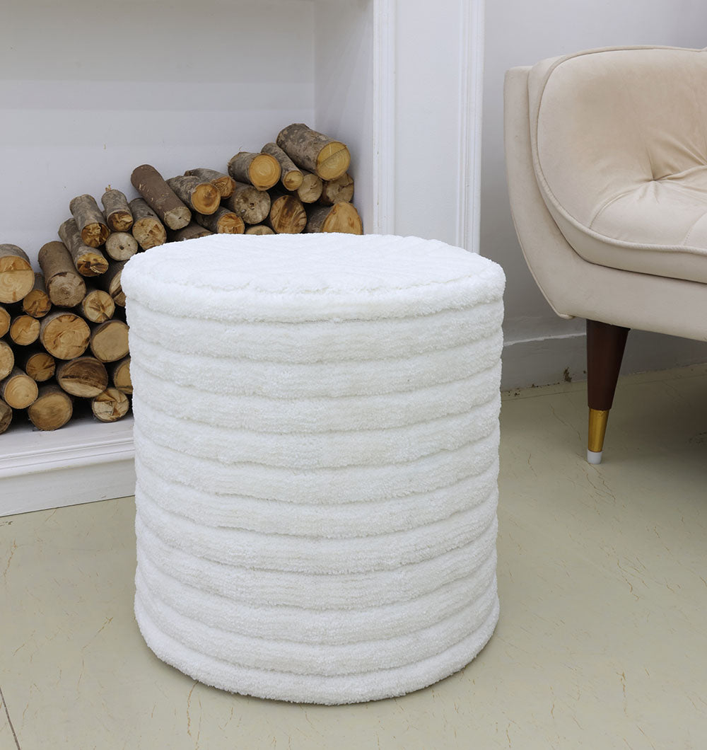 The RAMSHA HOME Luxury Handmade Pouf with Thermocol Bean Bag Insert PF-149, a round white textured piece, sits on a light floor by a beige armchair and stacked firewood, adding premium décor against the white wall.