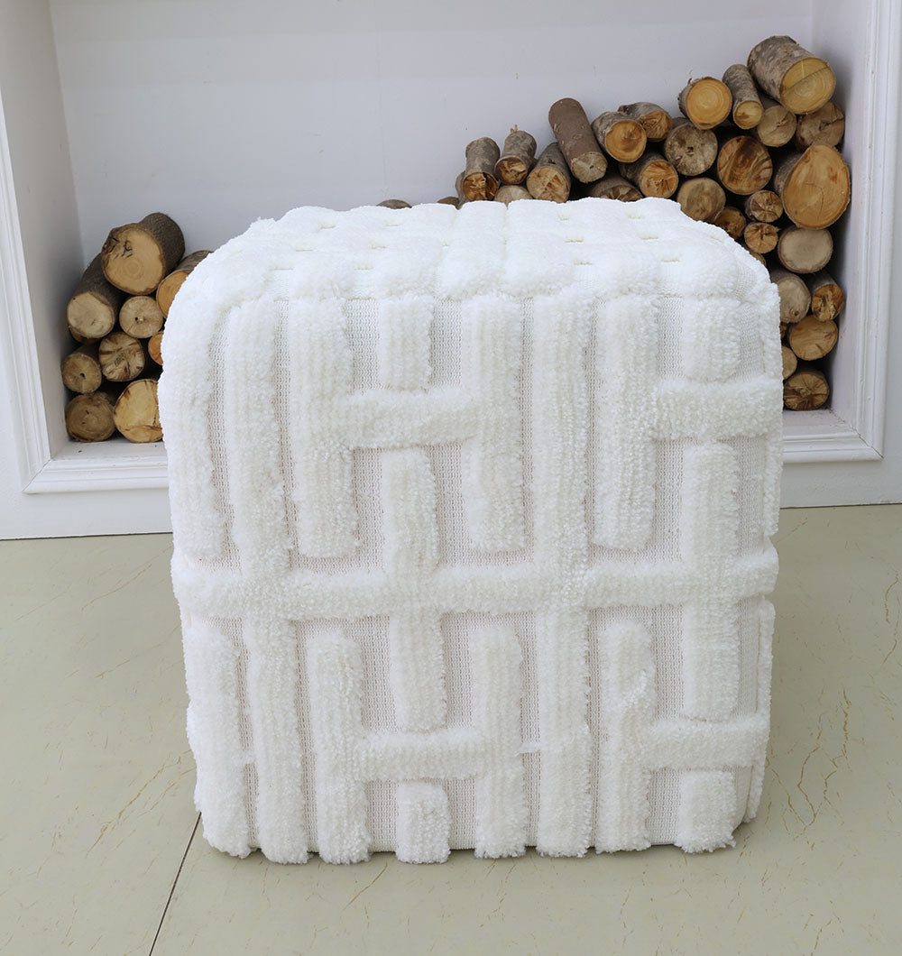 The RAMSHA HOME Luxury Handmade Pouf with Thermocol Bean Bag Insert PF-151, in white textured fabric and a raised geometric pattern, adds elegance in front of a fireplace filled with stacked logs on a light floor with a neutral background.