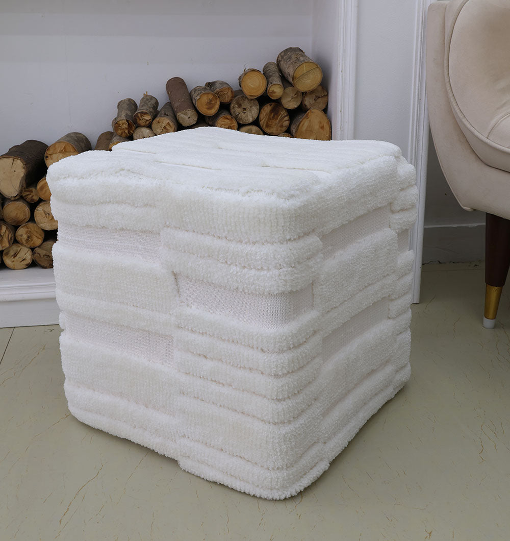 The RAMSHA HOME Handmade Pouf with Insert White Color PF-152—a white, square pouf with a soft layered design—sits on a light floor near log-filled fireplace and beige chair, perfect as premium home décor.