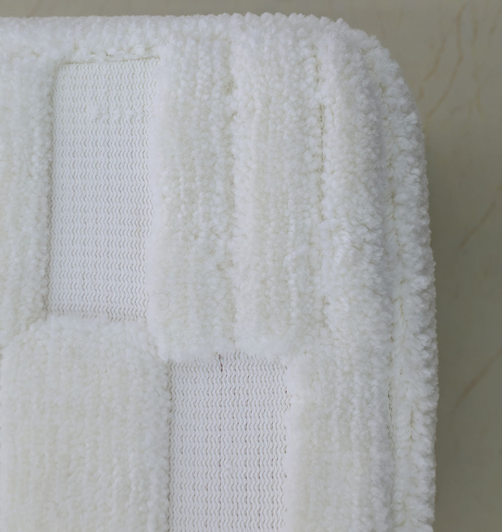 Close-up of a white, textured bath mat with a checkered pattern on a light-tiled floor—pairs perfectly with premium accents like the RAMSHA HOME Handmade Pouf with Insert White Color PF-152 for elevated home décor.