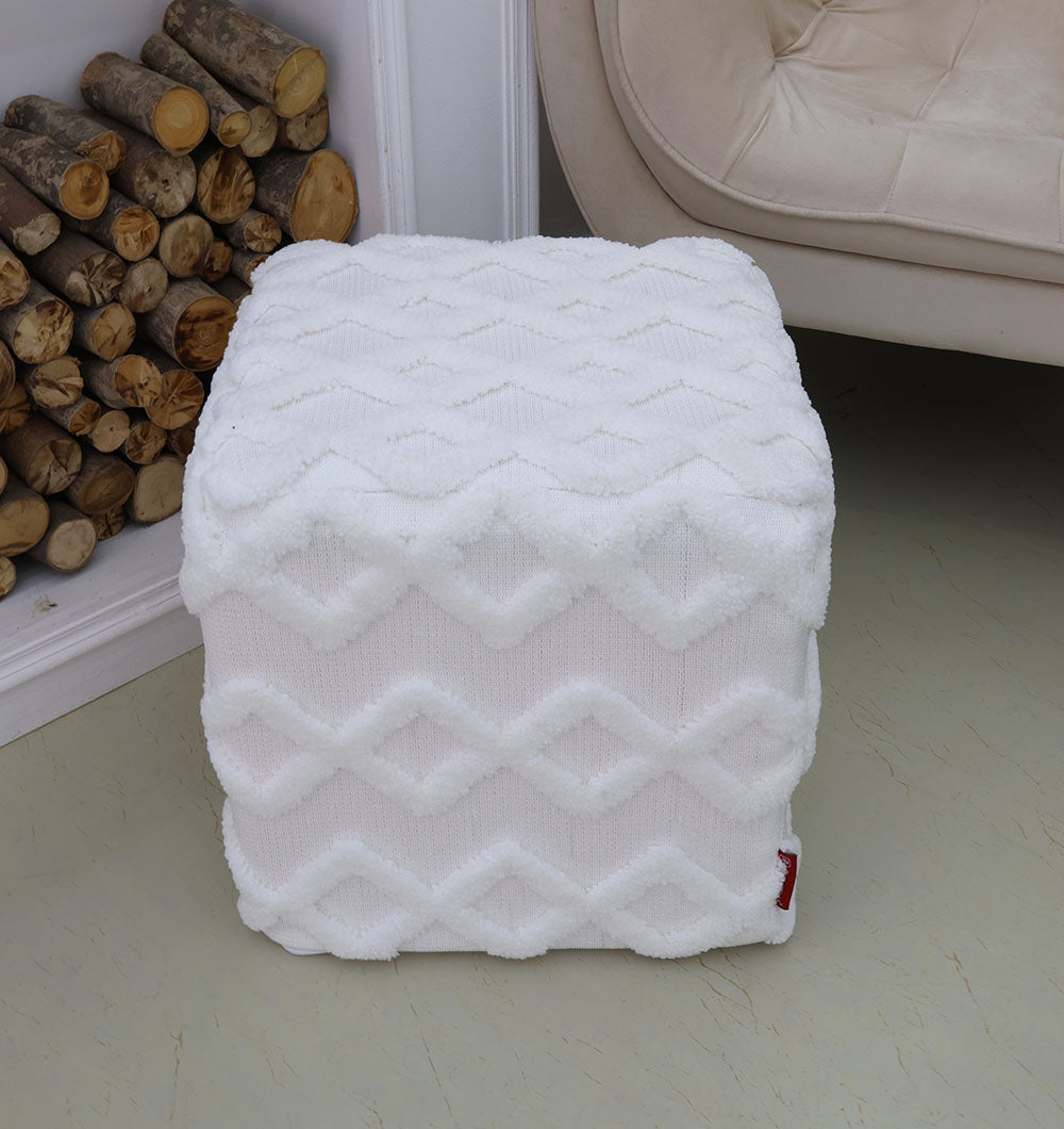 The RAMSHA HOME Handmade Pouf with Insert White Color PF-153, featuring a geometric pattern, is placed on a light floor near stacked firewood and a beige upholstered chair.