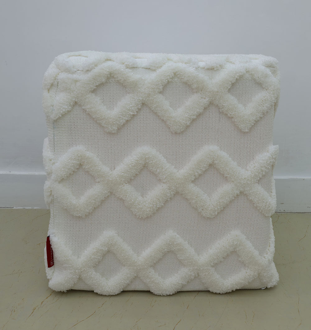The RAMSHA HOME Handmade Pouf with Insert White Color PF-153, featuring a textured raised diamond pattern and a small red tag, rests on a light tan floor against a plain white wall.