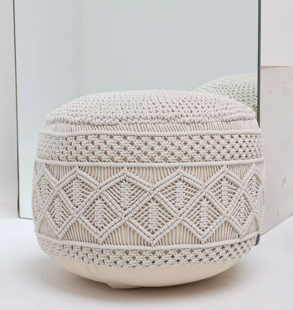 The RAMSHA HOME Boho Macrame Pouf White Round PF-156 features textured, woven geometric patterns and a detailed macramé design, sitting stylishly on a white floor in front of a large mirror.
