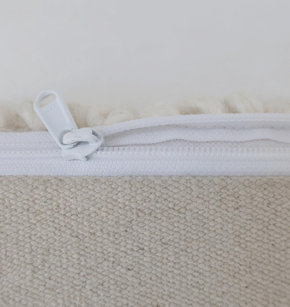 Close-up of a white zipper partially open on beige textured fabric of the RAMSHA HOME Handwoven White Macrame Pouf with Bean Bag Insert PF 162, revealing white material inside—ideal detailing for this cozy floor cushion.