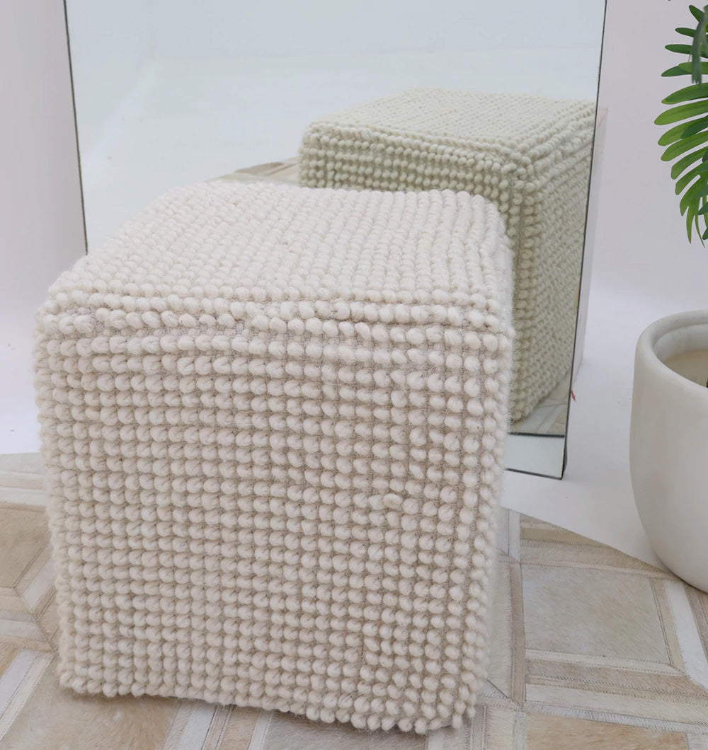 The RAMSHA HOME Handwoven White Macrame Pouf with Bean Bag Insert PF 162 sits before a mirror, its design reflected, and is placed beside a white planter holding a green plant on a patterned floor.