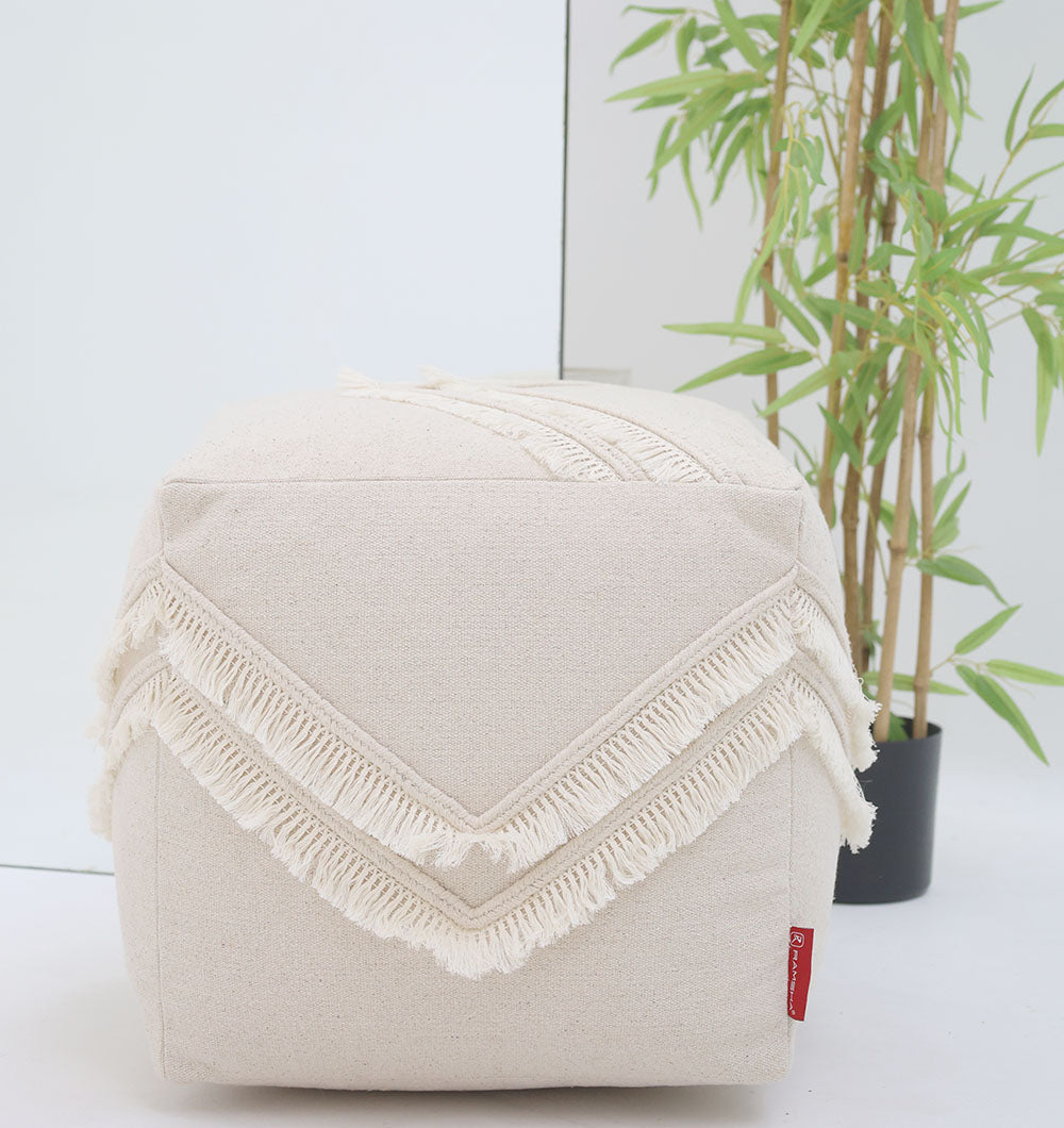 The RAMSHA HOME Ivory Handmade Cotton Pouf with insert PF 166 features decorative chevron fringes and elegant cream cotton, making it a stylish accent next to a mirror or bamboo plant on any white floor.