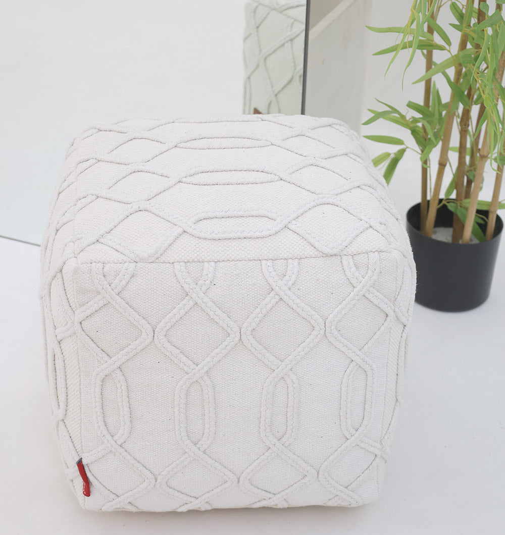 The RAMSHA HOME Ivory Nordic Bliss Cotton Pouf with insert PF 167 features a handmade geometric design, creating a stylish accent on a white floor near a mirror and potted plant.