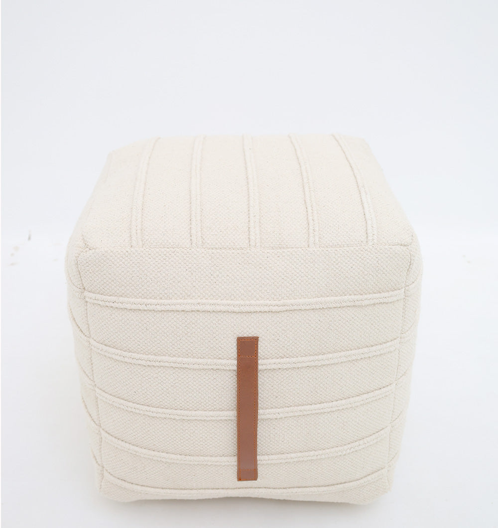 The RAMSHA HOME Ivory Nordic Bliss Cotton Pouf with insert PF 169 features a square, cream design, vertical stitched lines, and a brown leather strap, serving as a stylish decorative accent against a plain white background.