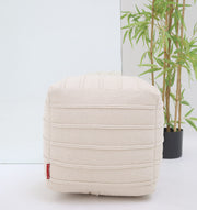 The RAMSHA HOME Ivory Nordic Bliss Cotton Pouf with insert (PF 169) sits before a mirror as a decorative accent. In the background is a potted bamboo, and a small red tag appears on the pouf’s lower left corner.