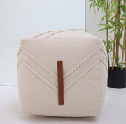 The RAMSHA HOME Ivory Nordic Bliss Cotton Pouf with insert PF 172, featuring a leather handle, adds an elegant accent to any room when placed near a potted plant and mirror on a white floor.
