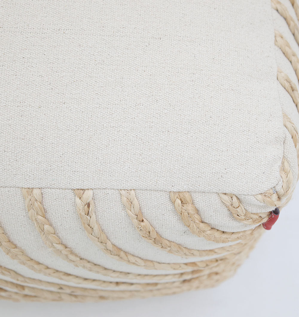Close-up of the Aurora Cotton Floor Pouf with insert PF 173 by RAMSHA HOME, handmade in beige cotton with thick braided rope accents along the edges and sides, shown resting on a light surface.