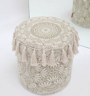 The Stylish cotton printed pouf with decorative tassels PF 174 by RAMSHA HOME, featuring intricate floral embroidery and beige boho design, is reflected in a mirror as it sits on a white floor.