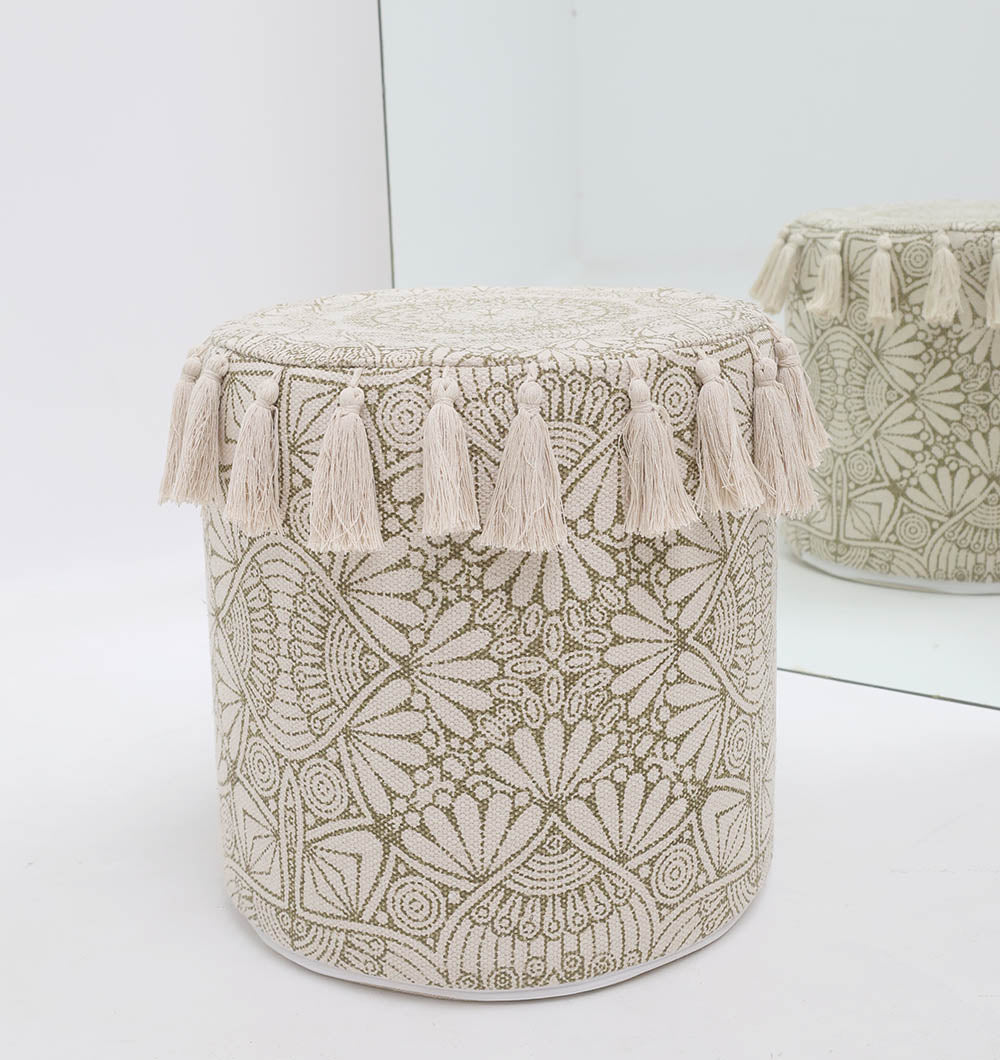 The RAMSHA HOME Stylish cotton printed pouf with decorative tassels (PF 174), featuring a round beige design and intricate embroidery, sits by a mirror, its chic boho floor cushion style and tassel accents beautifully reflected from the side.