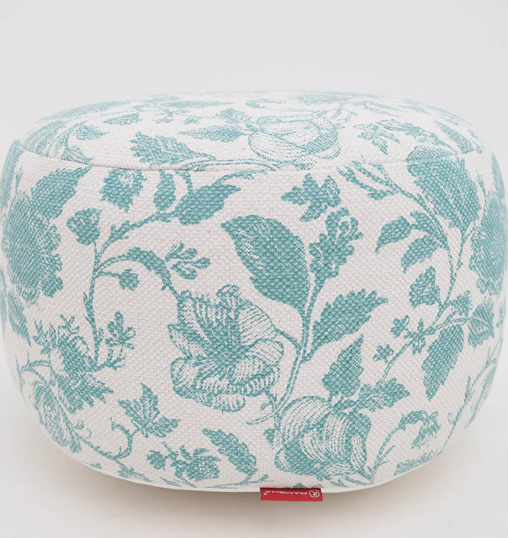 The RAMSHA HOME Round Bohemian Printed Pouf with Comfortable Insert PF 177 features white upholstery with a teal floral pattern and a red fabric tag for a stylish accent, offering both decorative seating and chic flair.