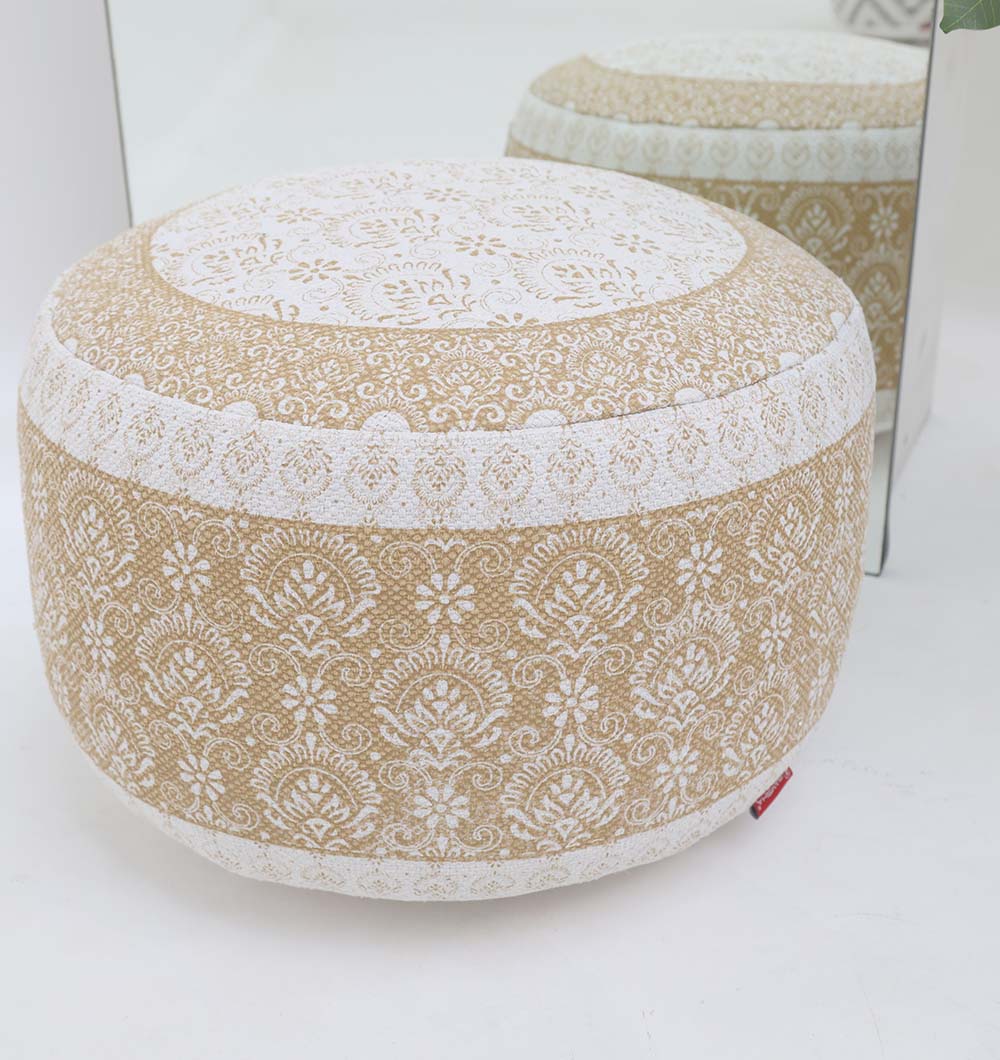 The RAMSHA HOME Round Bohemian Printed Pouf with Comfortable Insert PF 180, featuring a beige and white intricate pattern, sits on a white floor and is reflected in a nearby mirror, adding decorative seating to the room.