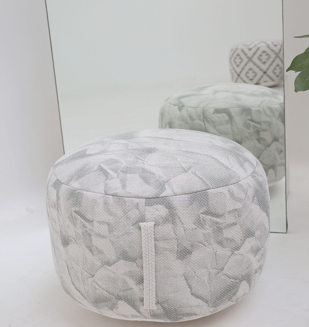 A round RAMSHA HOME Bohemian Printed Pouf with a comfortable insert (PF 182) features a vibrant floral design and sits by a mirror, its image reflected, while green leaves add elegance to the home décor.