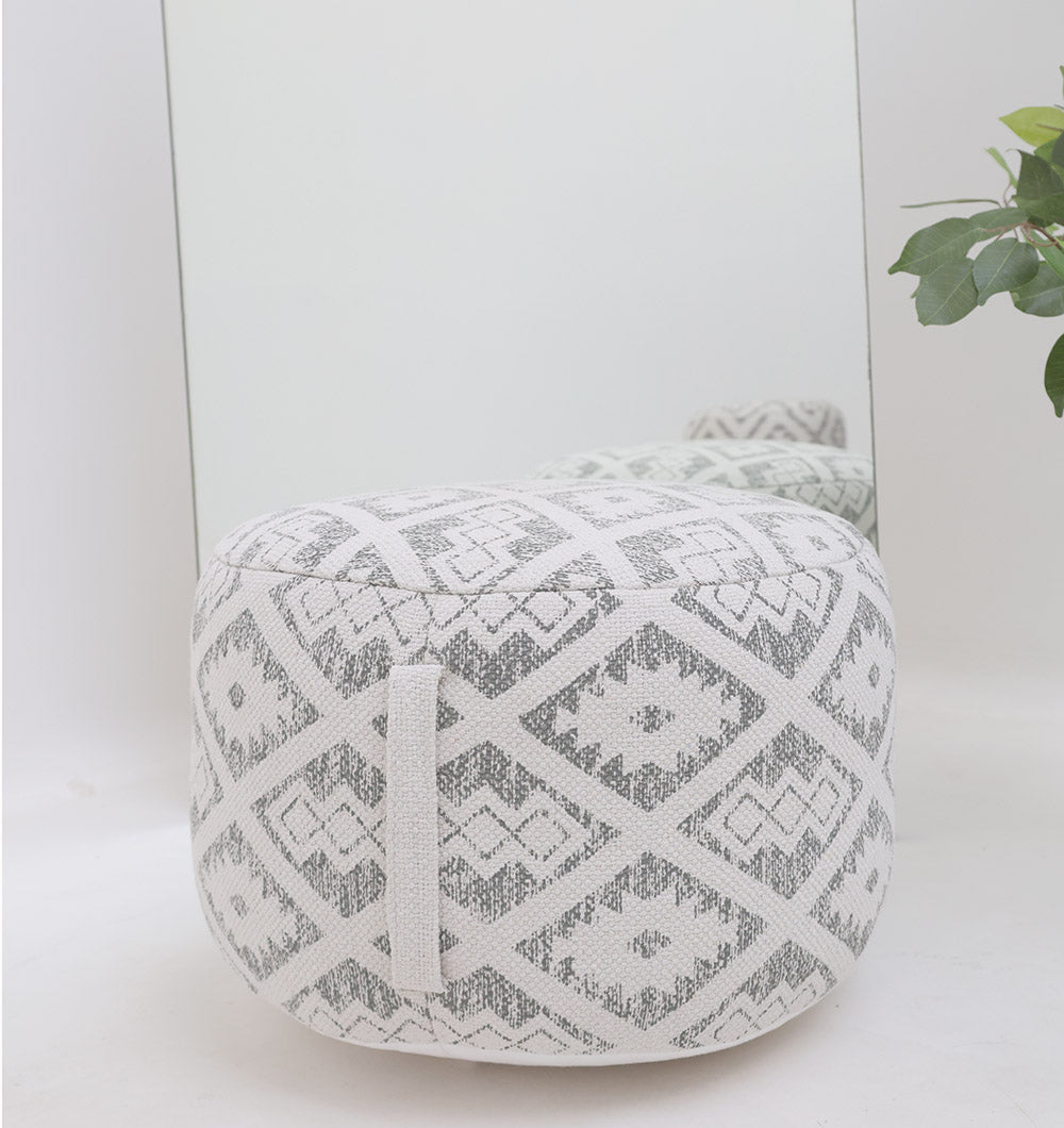 The RAMSHA HOME Round Bohemian Printed Pouf with Comfortable Insert PF 183 in light gray and white geometric diamond pattern sits stylishly in front of a mirror, complemented by a green leafy plant visible on the right.