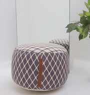 The RAMSHA HOME Modern Diamond Pattern Round Pouf with Comfortable Insert PF 184, in purple and white with a brown handle, sits before a mirror. A green leafy plant on the right adds an inviting touch to your home décor.