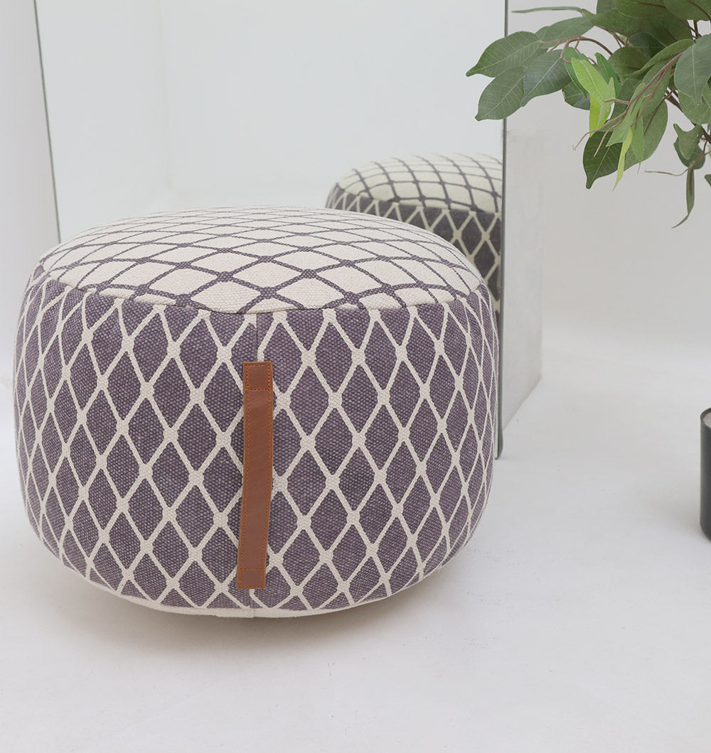 The RAMSHA HOME Modern Diamond Pattern Round Pouf with Comfortable Insert PF 184 sits on a white floor by a glass mirror, adding stylish charm to your décor. A leafy green plant is partially visible in the upper right corner.
