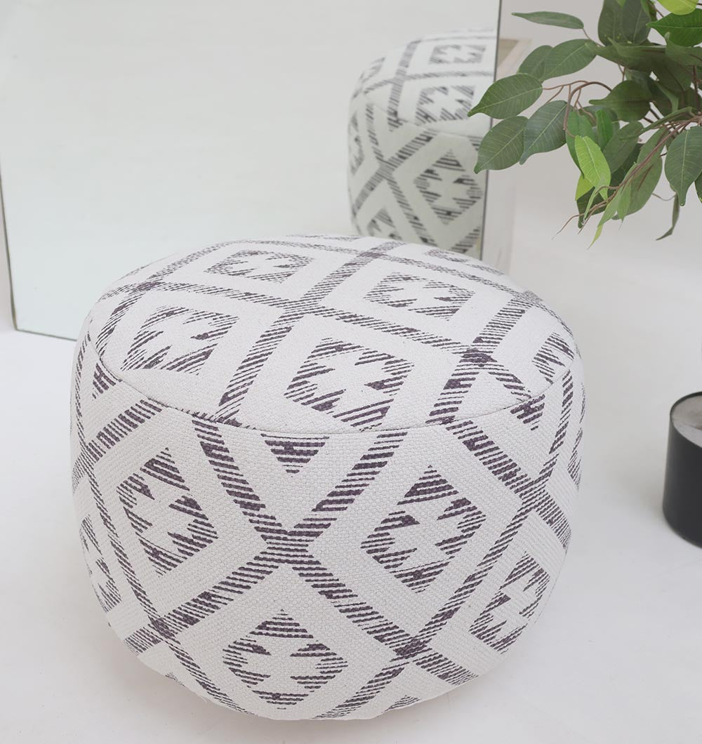 The RAMSHA HOME White Color Modern Diamond Pattern Round Pouf with Insert PF 185 sits on a white floor near a mirror and a potted plant, adding stylish flair as both the pouf and its modern pattern are reflected in the mirror.