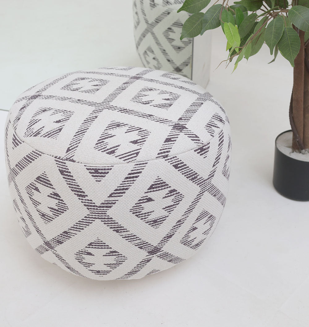 The RAMSHA HOME White Color Modern Diamond Pattern Round Pouf with Insert PF 185 sits on a white floor next to a potted green plant. Another pouf and plant are partially visible in the background.