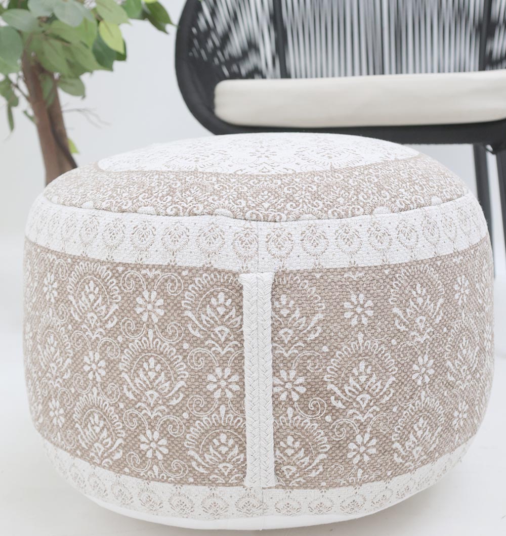 The RAMSHA HOME Modern Printed Round Pouf with Insert PF 186, featuring beige and white floral designs, adds a stylish accent to your modern décor when placed beside a plant and black chair in a minimalistic room.