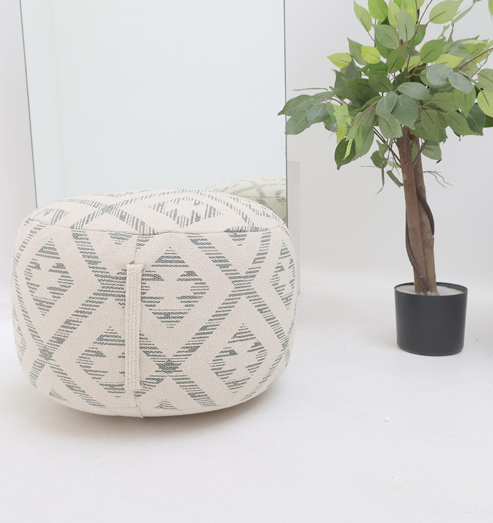 The Round Bohemian Printed Pouf with Comfortable Insert PF 188 by RAMSHA HOME, in beige and gray, adds style beside a potted artificial tree on a white floor, beautifully reflected in a mirror—ideal for enhancing your home décor.