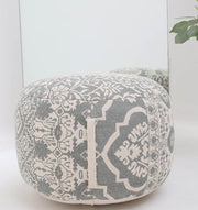 The RAMSHA HOME Bohemian Grey Color Printed Pouf with Comfortable Insert PF 189 sits in front of a mirror, its stylish design reflected. Ideal for home décor, complemented by greenery from a plant on the right side.