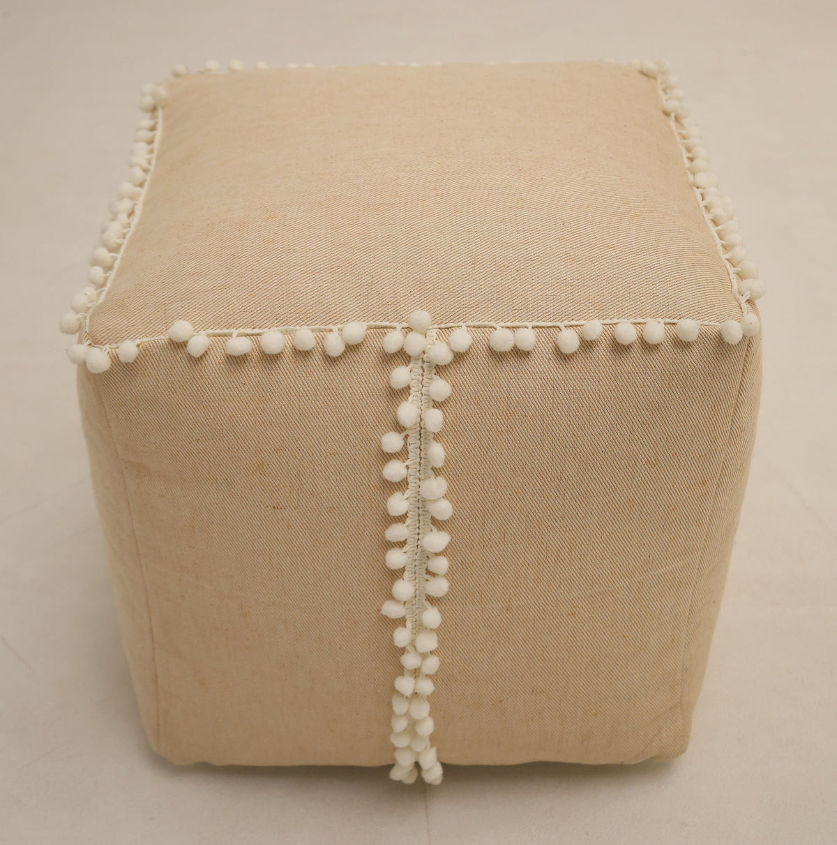 The RAMSHA HOME Square Jute Floor Pouf with Fringes PF 193, featuring textured beige jute fabric and delicate fringe detailing along the seams, sits atop a light-colored floor and serves as a charming accent piece that adds subtle interest to any room.