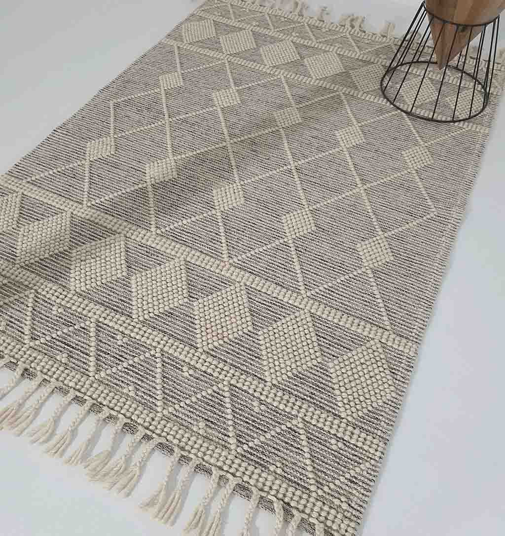 The RAMSHA HOME Fringes Woven Rug For Indoor, Floor Rug SRN-017 in beige and off-white with a geometric diamond pattern and fringed edges is displayed on a white floor, with part of a wire-base table in the upper right corner.