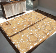 The RAMSHA HOME Braided Natural Outdoor Jute Rug (BR 086), featuring a sunburst design in brown and tan, sits on a light floor beside a white cabinet with wooden top, sunlight streaming into the minimalist room.