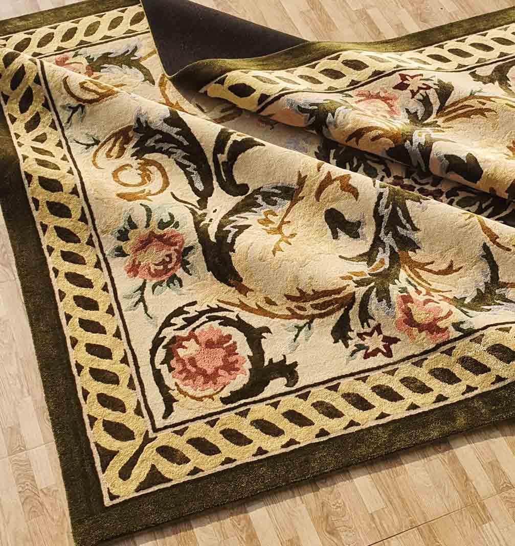 The RAMSHA HOME Luxurious Wool, Silk & Cotton Handmade Rug - HTWV 03 (300x400cm) features a detailed beige, green, and pink floral and leaf pattern. Partially folded on a light wood floor, its intricate border and traditional design are visible.