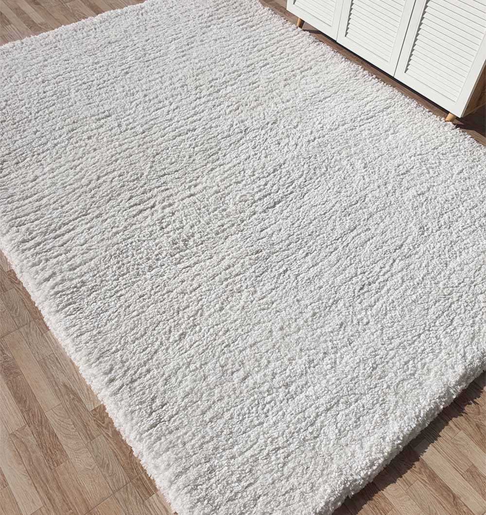 The RAMSHA HOME Soft White Rectangle Bedroom Rug - SG 06, featuring a shaggy, plush pile, lies on a wooden floor beside a white cabinet with shutter-style doors.