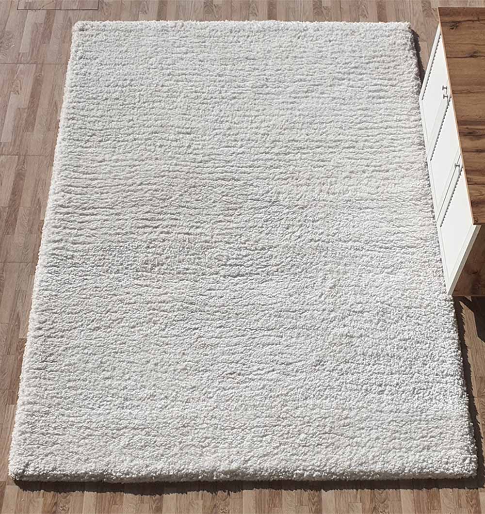 The RAMSHA HOME Soft White Rectangle Bedroom Rug - SG 06, a shaggy rug with a soft pile, lies on the wooden floor beside a wooden cabinet with white doors.