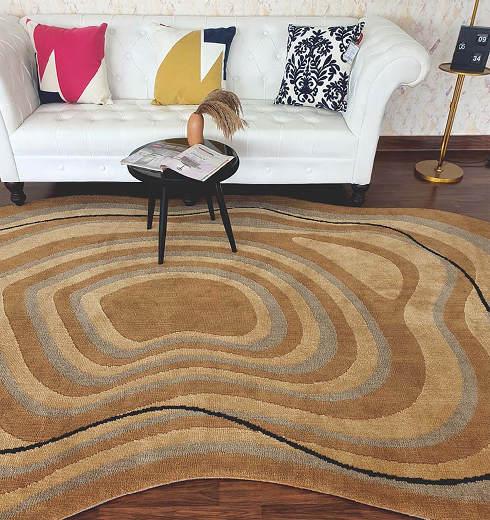 A modern living room with a white tufted sofa, colorful geometric and floral cushions, side tables, and the RAMSHA HOME Curved Shaped Multi Colored Carpet CMN-08 in brown and beige on wooden flooring.