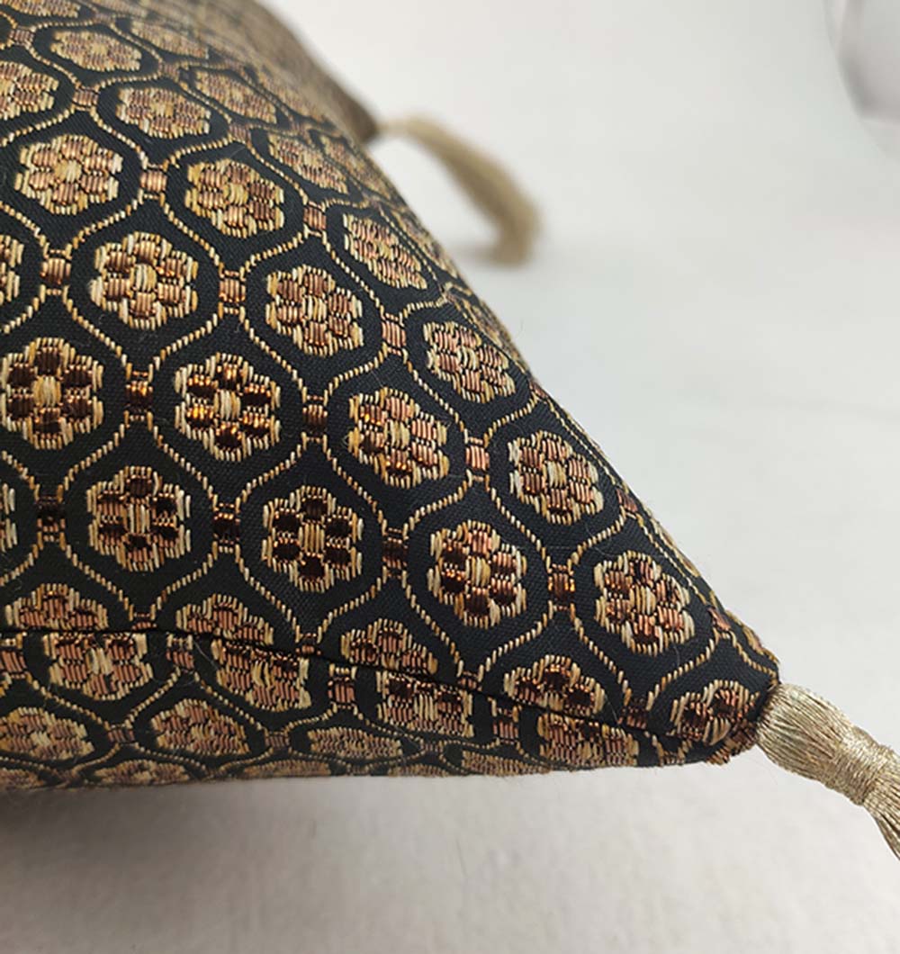 The RAMSHA HOME Polyester Cushion Black And Gold With Tassel features a plush texture, intricate geometric pattern, and a black and gold corner tassel, shown close-up against a white background.