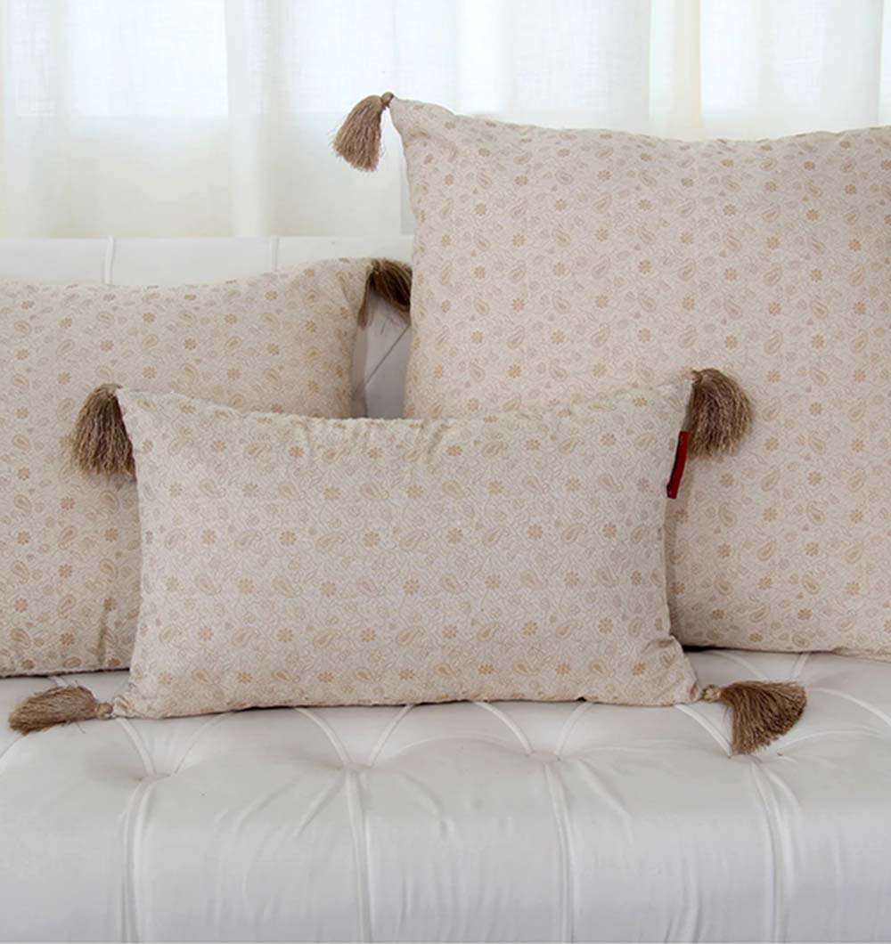 Three RAMSHA HOME Polyester Cushions in black and gold with tassels are arranged on a white tufted sofa, set against a sheer white curtain in the background.