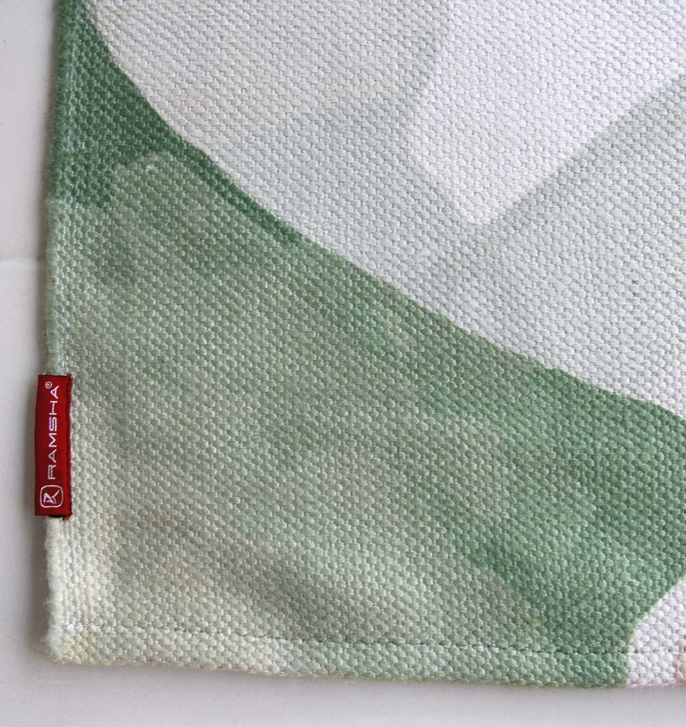 A close-up of the Floral Printed Area Rug Multi Color 150x210 cm DD-031 shows textured fabric with green and white patterns. A small red tag with the brand name RAMSHA HOME is stitched to the corner.