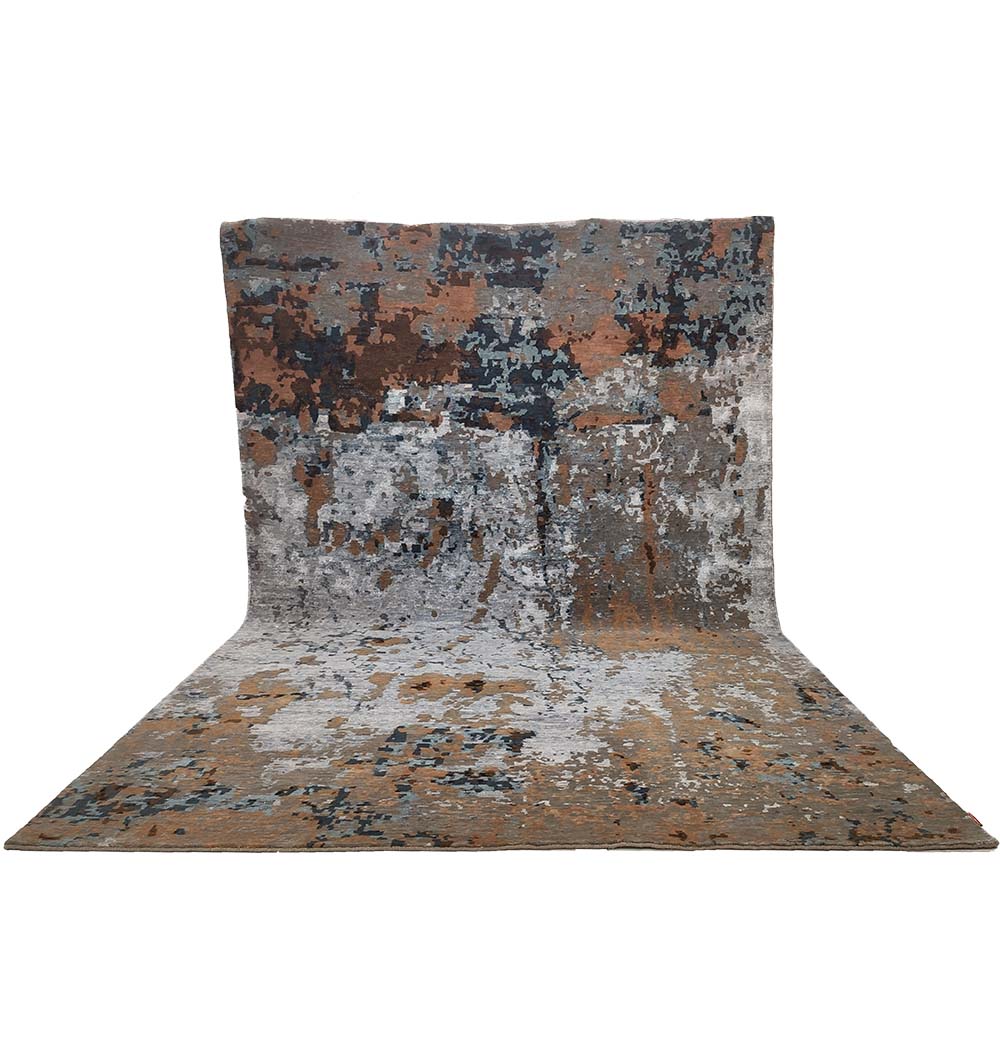 The RAMSHA HOME Bamboo Silk & Cotton Hand Knotted Carpet HKWB-012, featuring an abstract pattern in brown, gray, white, and blue tones, is draped vertically and curves seamlessly from the wall onto the floor.