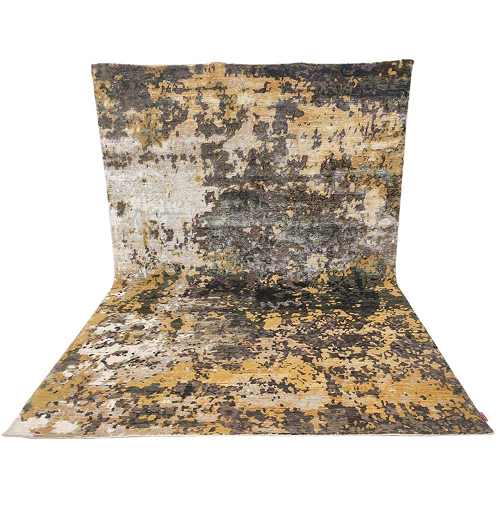 The RAMSHA HOME Bamboo Silk & Cotton Carpet HKWB-014 features a modern abstract design in yellow, brown, gray, and black shades, shown draped vertically and extending onto the floor.