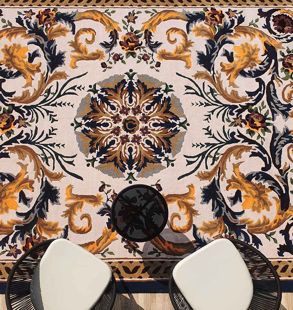 Two modern white chairs and a small round table sit on the RAMSHA HOME Polyester & Cotton Hall Decor Rug - HTP 02 (300x400cm), featuring an intricate scroll design—perfect for adding classic charm to your space.