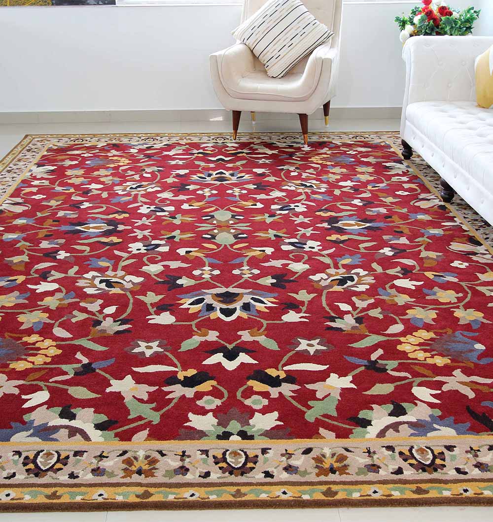 The RAMSHA HOME Wool & Cotton Handmade Area Rug HTW-08, featuring a traditional floral pattern in rich reds, covers the bright living room floor, framed by a white armchair with pillows, a white sofa, and a small vase of flowers in the corner.