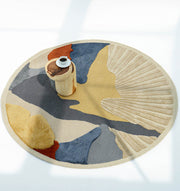 The RAMSHA HOME Multicolor Handmade Round Rug HTW 59 (200cm) features abstract patterns in beige, blue, yellow, grey, and rust. A wooden cylinder with a cup and saucer sits on the hand-tufted rug, illuminated by natural light.